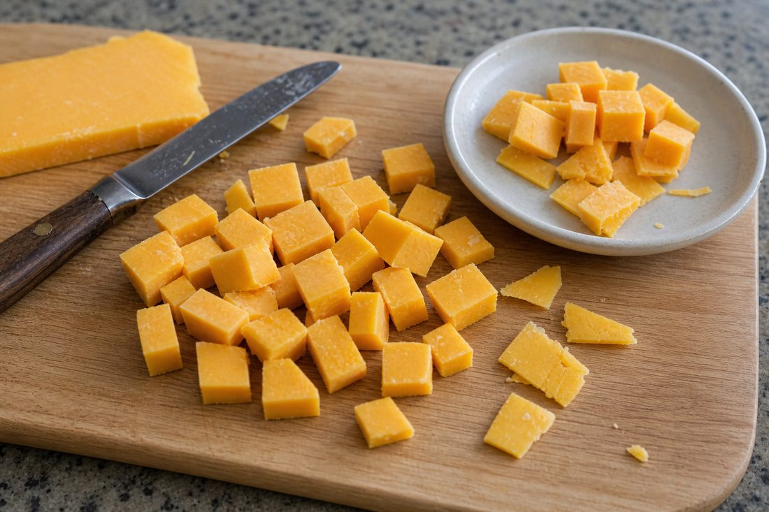 Sharp cheddar cut into small cubes and thick pieces on a cutting board.