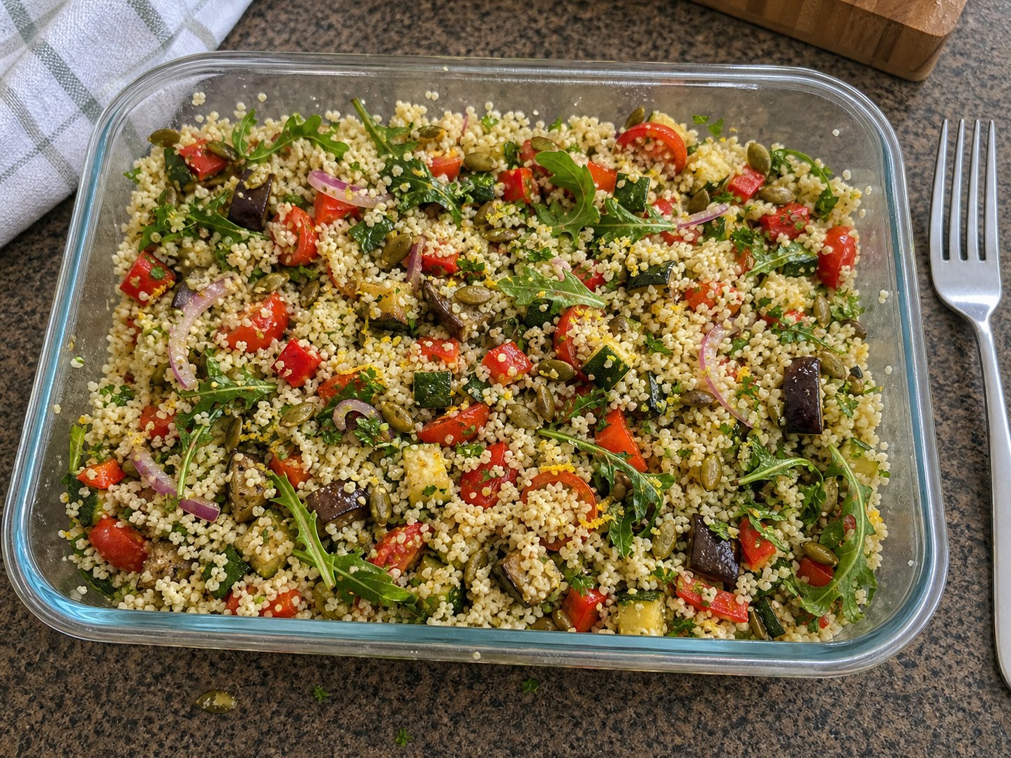 Finished couscous roasted vegetable salad lightly mixed with arugula, lemon tahini dressing, pumpkin seeds, herbs, and roasted vegetables.