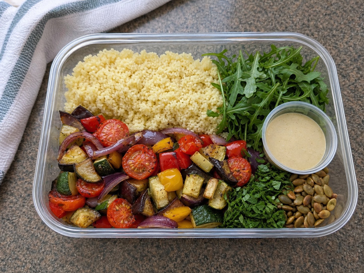 Unmixed couscous roasted vegetable salad packed with couscous, roasted vegetables, arugula, lemon tahini dressing, pumpkin seeds, and herbs.