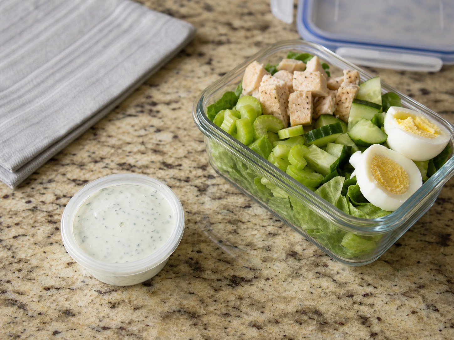 Small sealed cup of Greek yogurt ranch packed beside an undressed work salad.