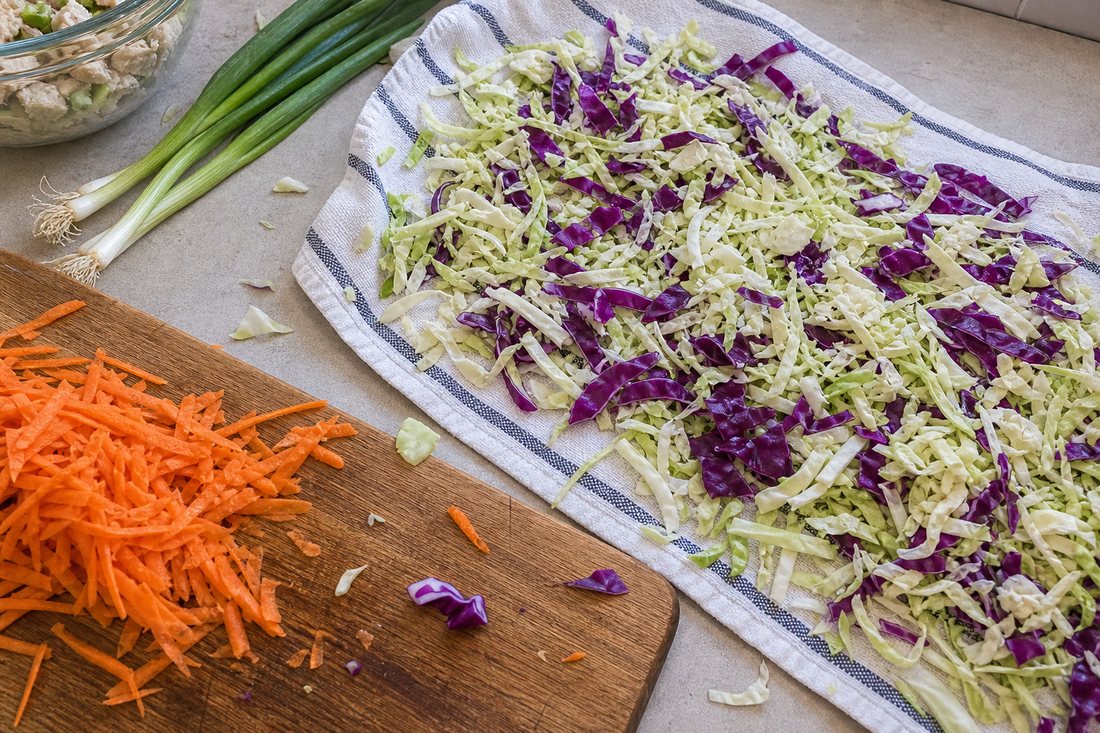 Shredded cabbage and carrots spread on a towel and cutting board before packing.