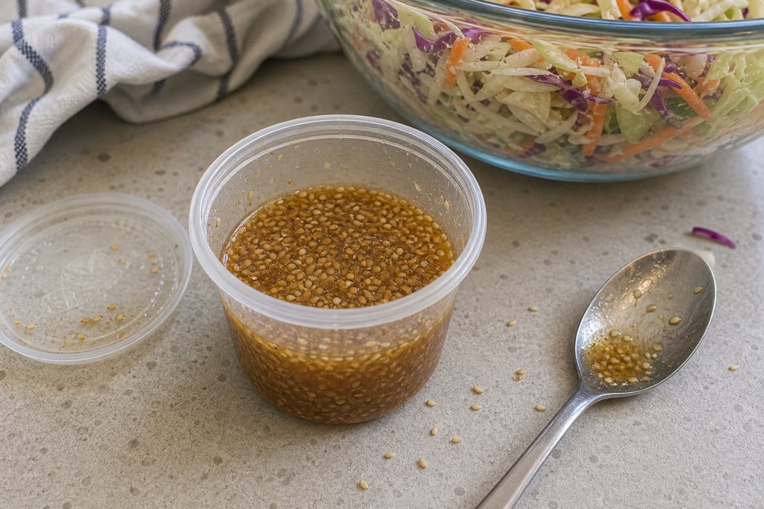 Small cup of ginger sesame dressing beside cabbage carrot slaw.
