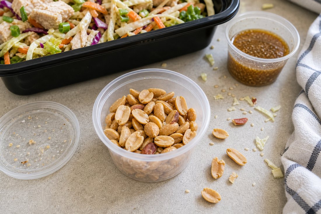 Roasted peanuts packed in a small separate cup beside a crunchy chicken cabbage salad.
