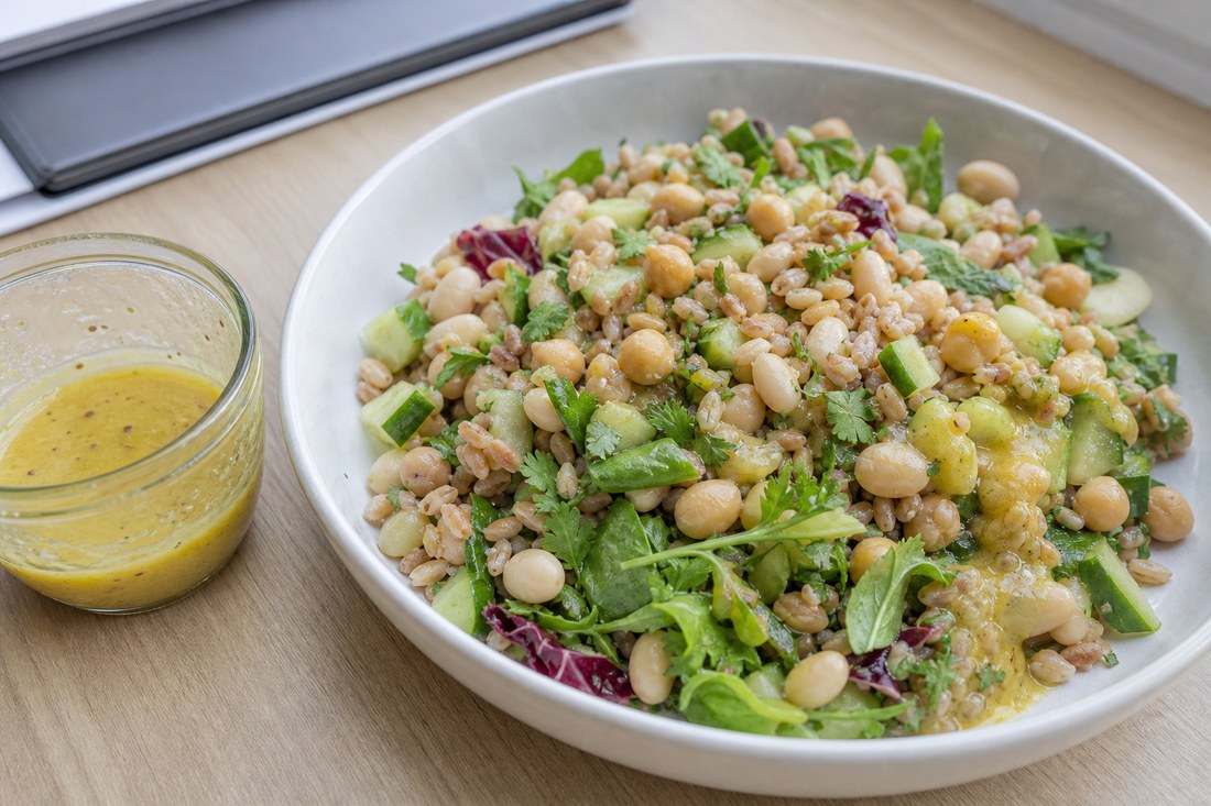 A bean and grain salad with a small cup of yellow lemon Dijon dressing added only to one side.