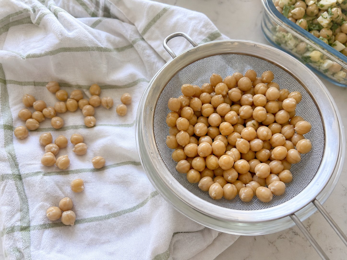 Rinsed chickpeas draining in a strainer and drying on a towel before egg and chickpea protein salad.