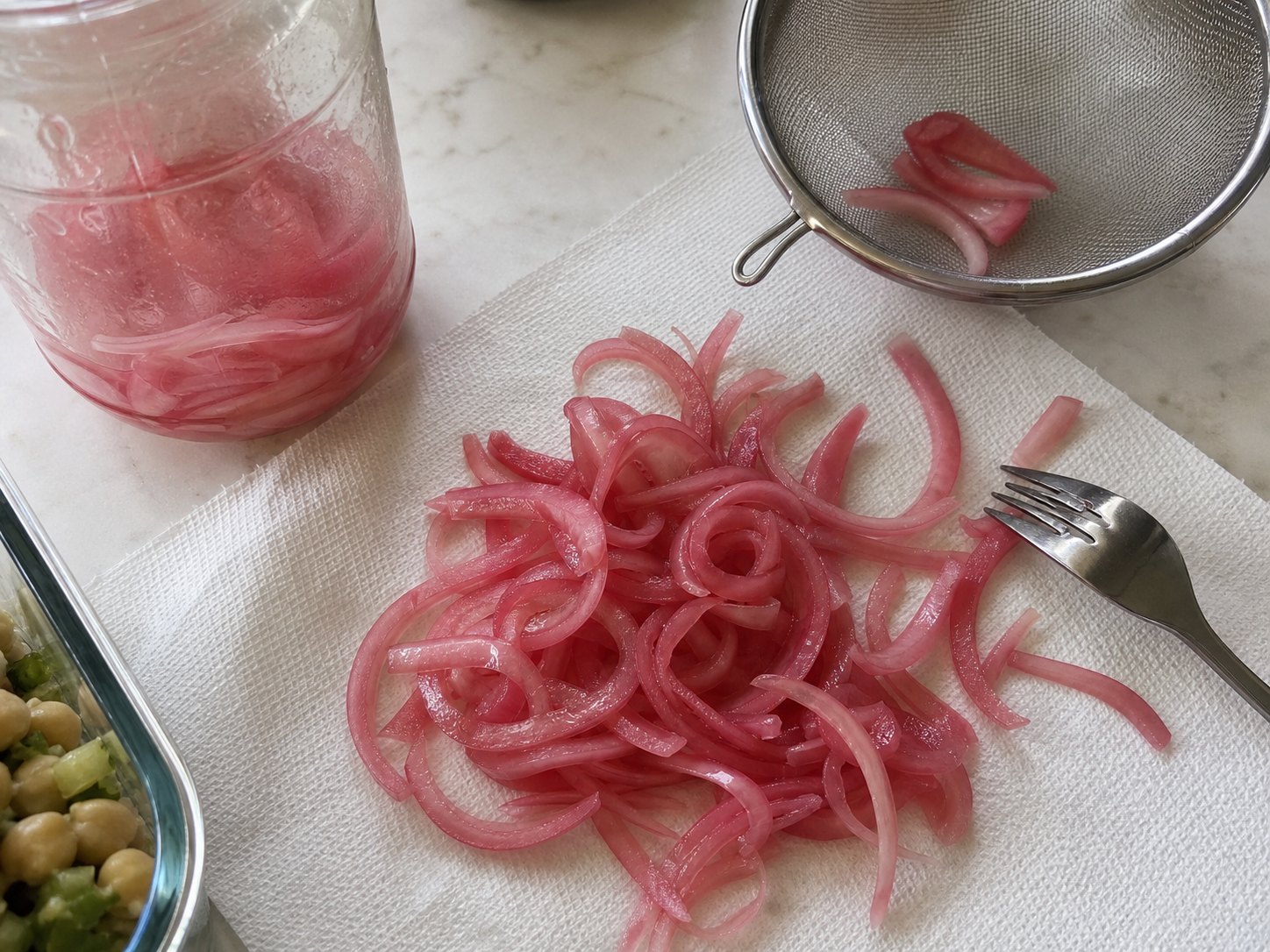 Drained pickled red onions on a towel with a small strainer before egg and chickpea protein salad.