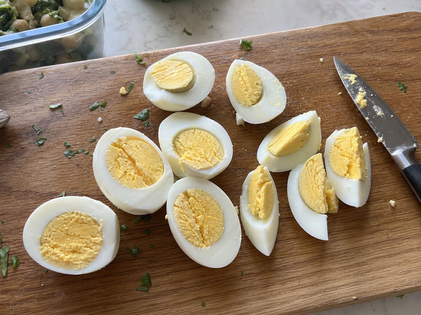 Hard-boiled eggs cut into large halves and wedges on a cutting board for egg and chickpea protein salad.