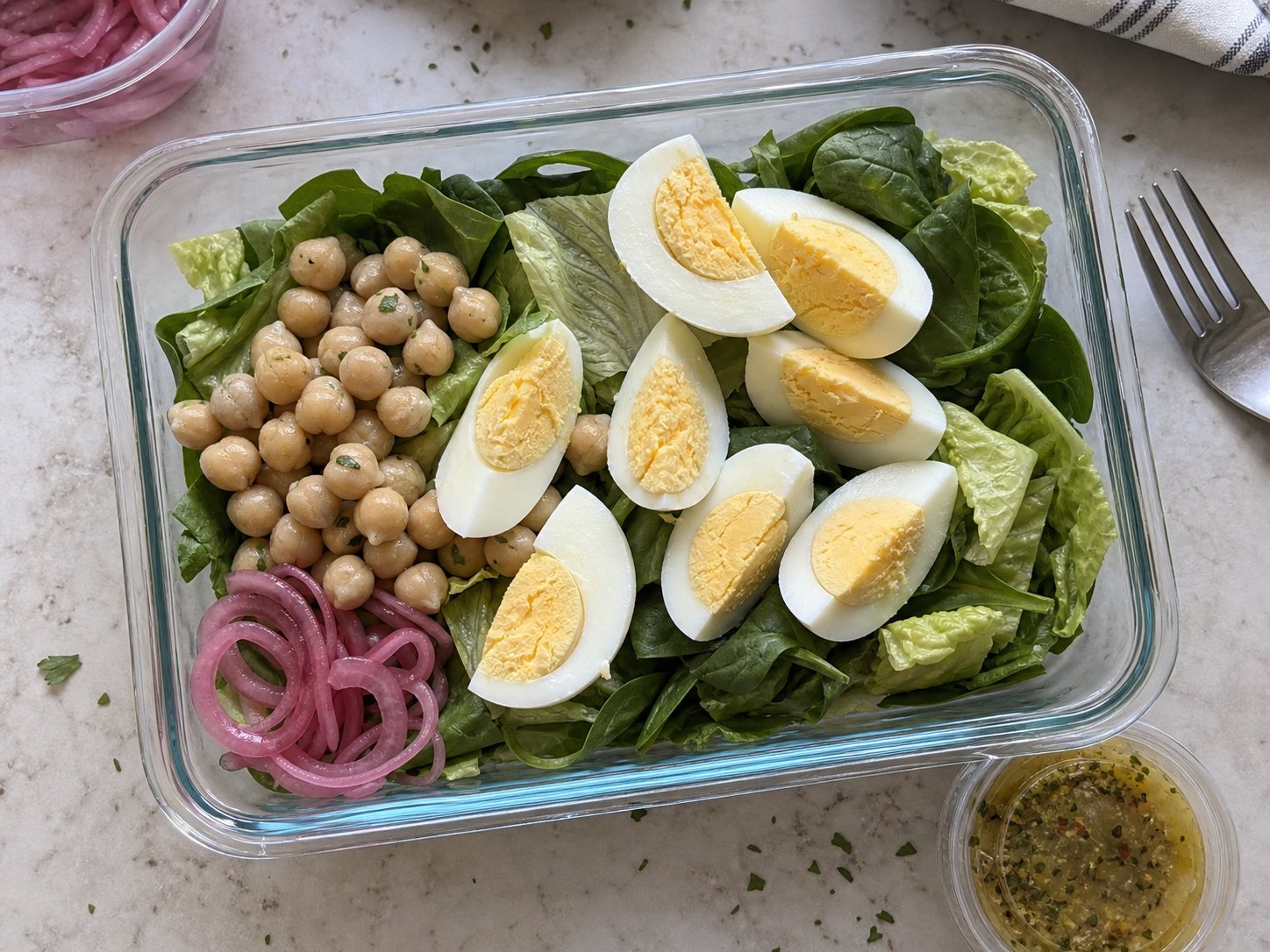 Unmixed egg and chickpea protein salad packed with spinach, romaine, chickpeas, egg wedges, pickled onions, and mustard herb dressing cup.