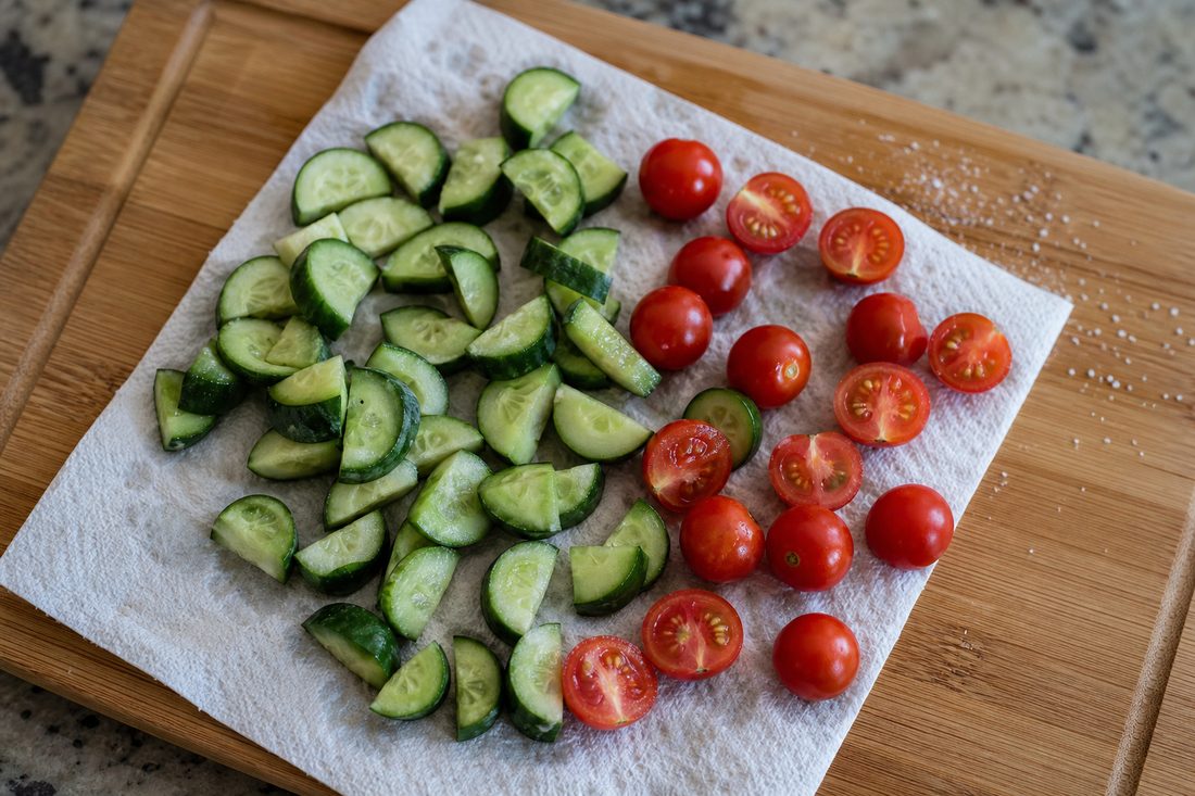 Cut cucumber and cherry tomatoes resting on a towel before packing a Greek chicken salad lunch box.