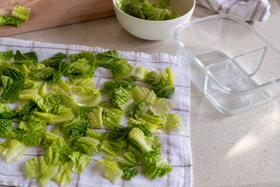 Chopped romaine spread on a towel beside a lunch container before packing.