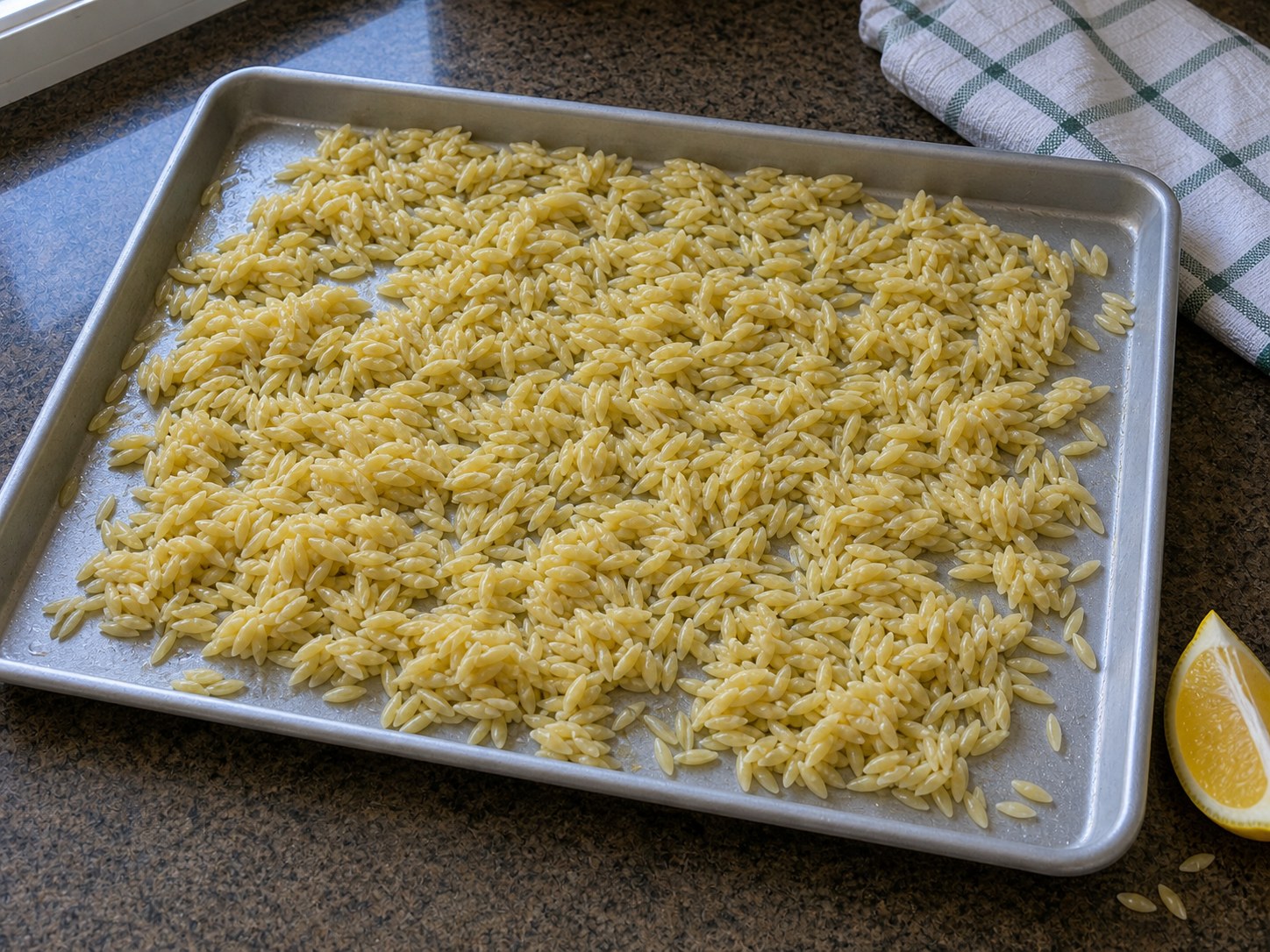 Cooked orzo spread on a sheet pan to cool for Greek orzo chickpea salad.