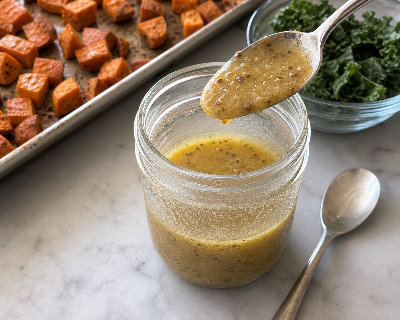 Chilled maple mustard dressing clinging lightly to a spoon in a glass jar.