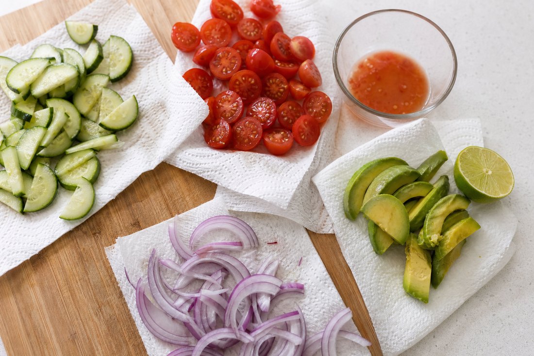 Cucumber, tomatoes, avocado, and red onion kept on towels and separate from greens.