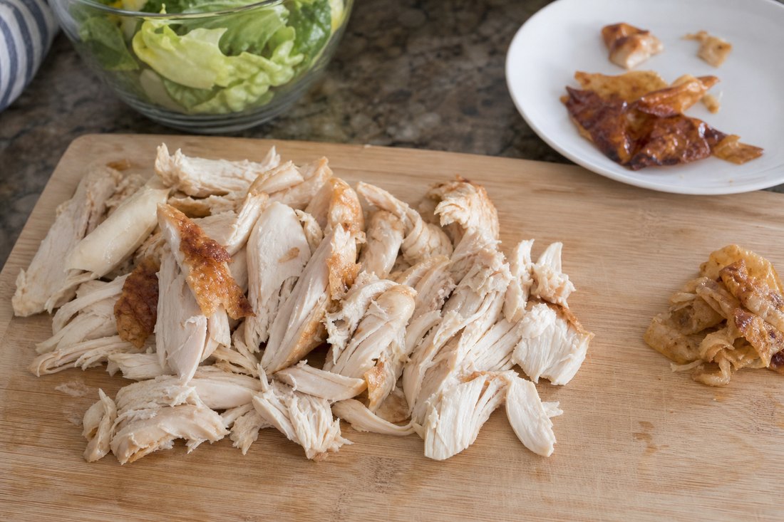 Rotisserie chicken pieces with a few browned skin edges set aside for salad.