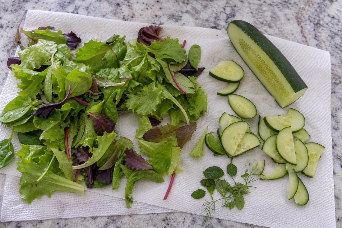 Dry mixed greens and cucumber slices prepared for a rotisserie chicken salad.