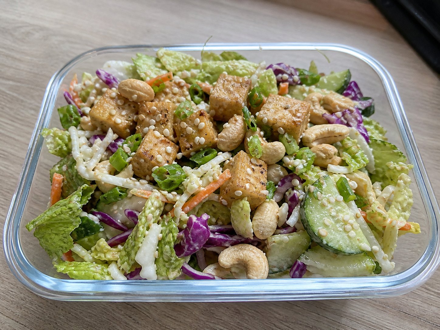 Finished sesame tofu cabbage salad lightly dressed with cashews, sesame seeds, scallions, cabbage, cucumber, carrot, and golden tofu.