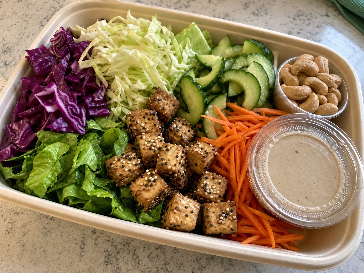 Unmixed sesame tofu cabbage salad packed with cabbage, romaine, carrot, cucumber, golden tofu, cashews, and dressing cup.