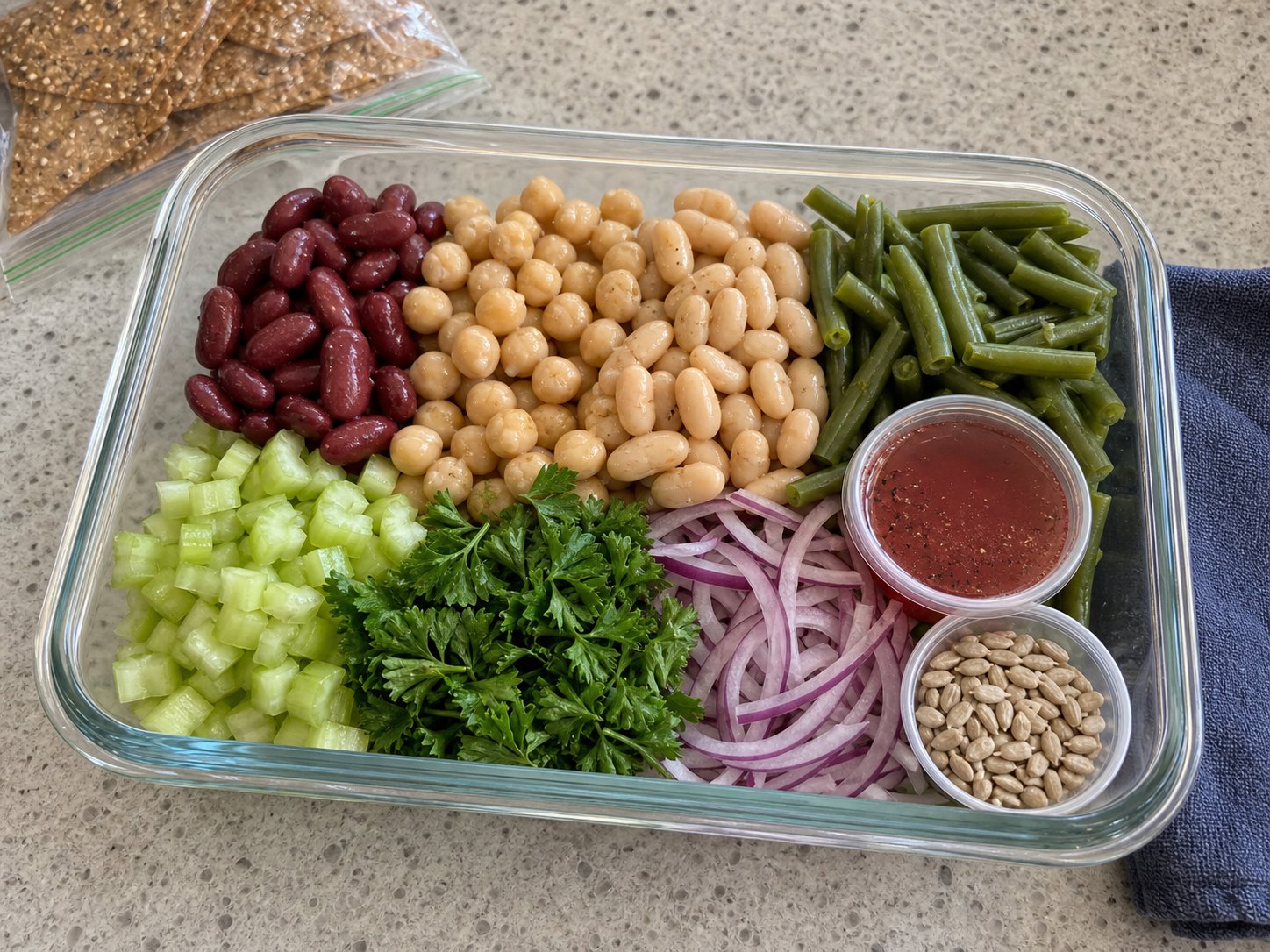 Unmixed three-bean picnic salad packed with kidney beans, chickpeas, white beans, green beans, celery, parsley, red onion, red wine vinaigrette cup, and sunflower seeds.