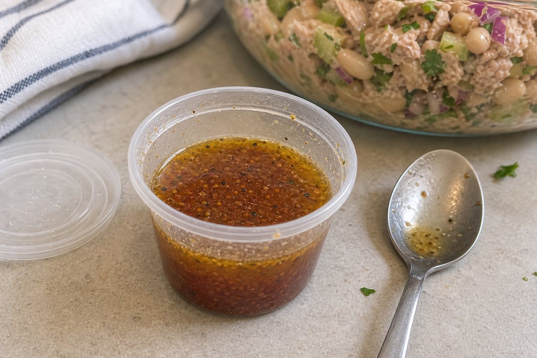 Small cup of red wine vinaigrette beside tuna white bean salad ingredients.