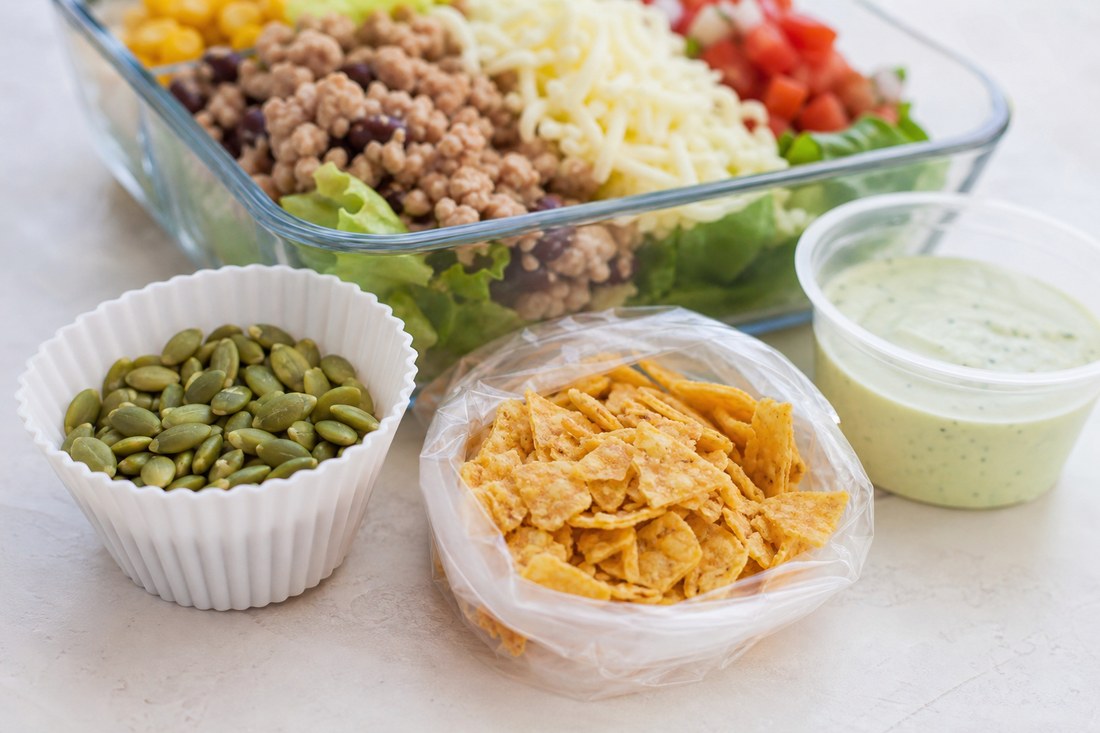 Pepitas and crushed tortilla chips packed separately from turkey taco meal prep salad.